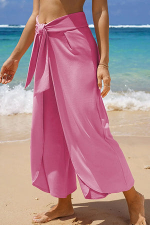 Pink wrap-front palazzo pants with slit hem and tie waist detail.