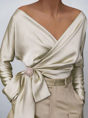 Draped satin blouse in cream with V-neck, brooch detail, and tie waist.