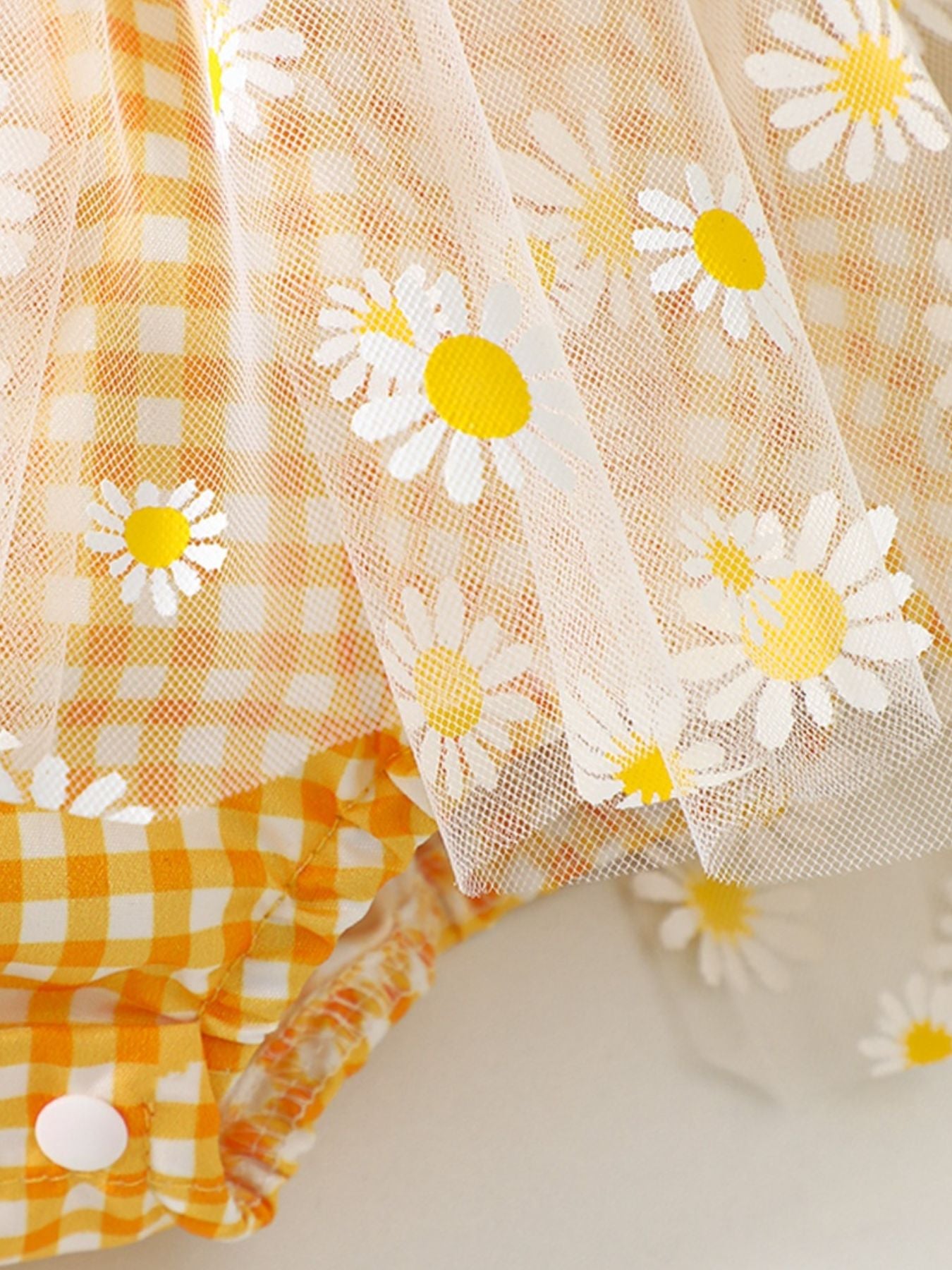 Yellow gingham baby one-piece with daisy-print tulle overlay and ruffle trim.