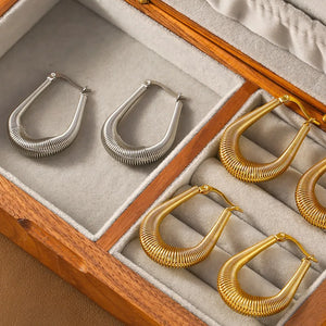 Coiled oval hoop earrings in gold and silver, featuring a unique spring-like texture.
