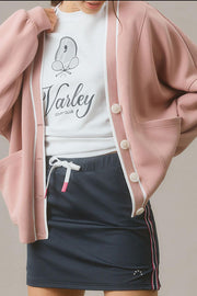 Dusty pink cocoon cardigan with white trim and buttons, styled casually.