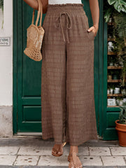 Brown textured smocked waist wide-leg trousers with drawstring and pockets.