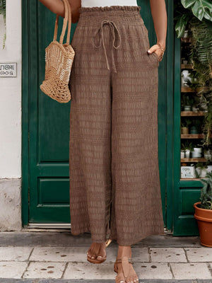 Brown textured smocked waist wide-leg trousers with drawstring and pockets.