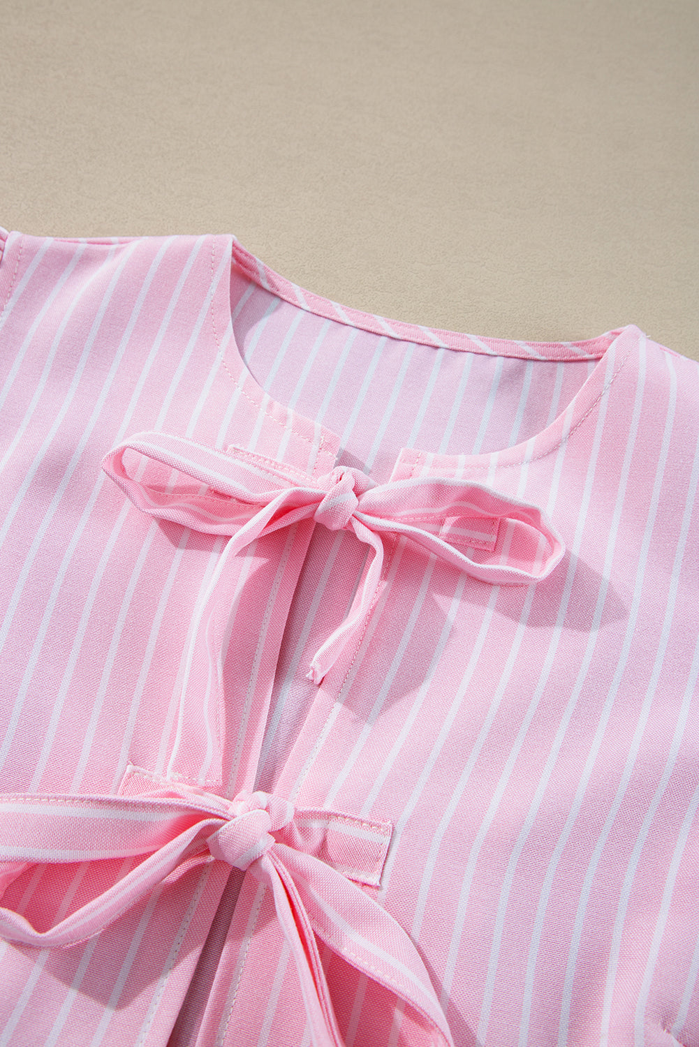 Blush pink striped peplum blouse with bow embellishments at the neckline and waist.