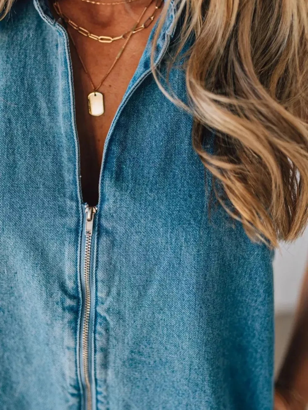 Denim romper with zipper closure and layered necklaces.