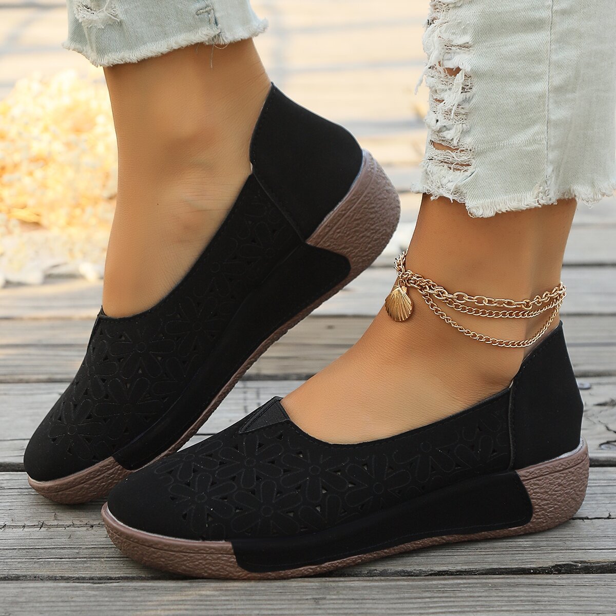 Black floral cutout slip-on loafers with a brown sole and a seashell anklet.