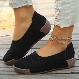 Black floral cutout slip-on loafers with a brown sole and a seashell anklet.