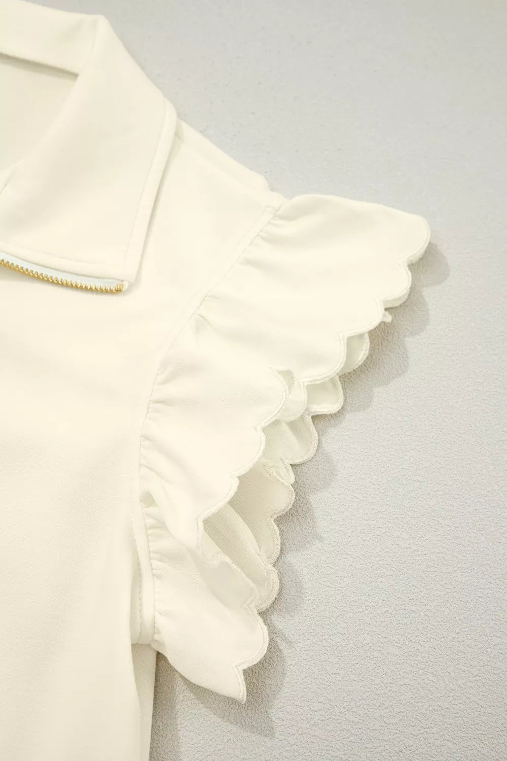 Cream cotton blouse with stand-up collar, zip front, and ruffled scalloped cap sleeves.