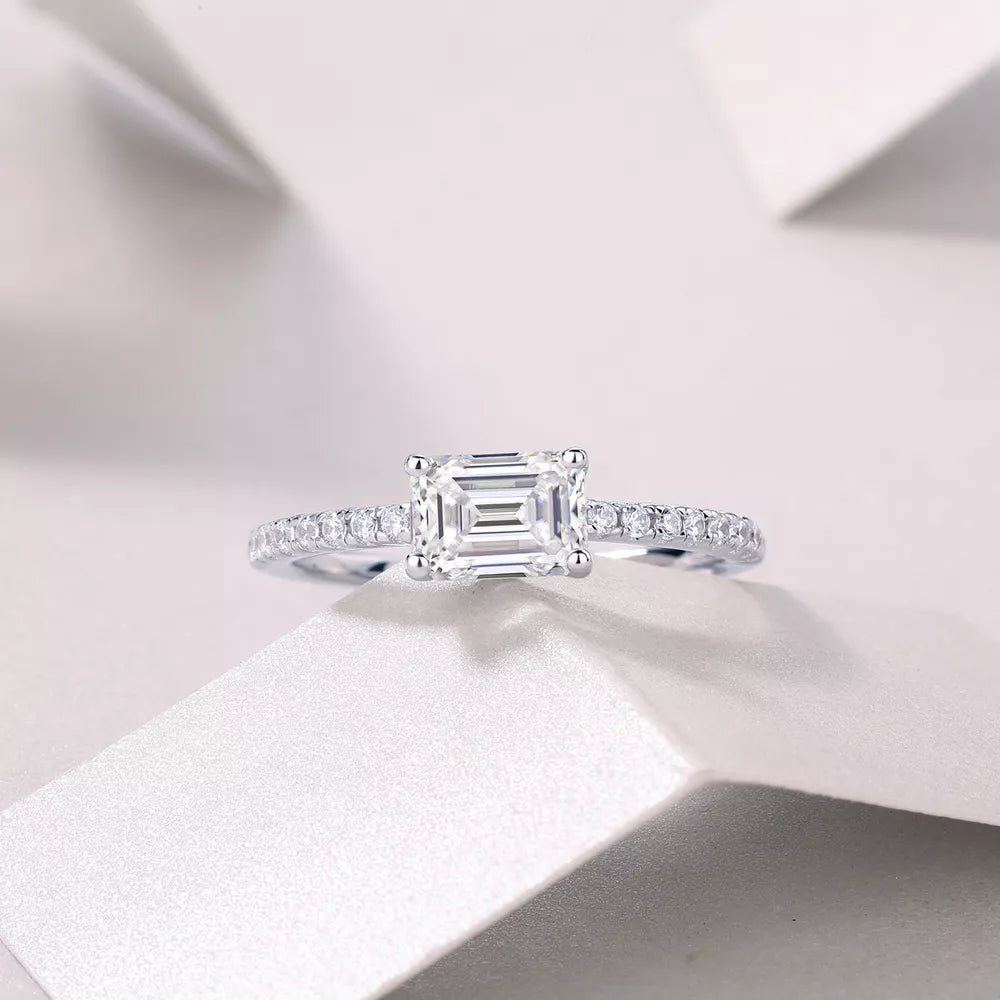 Elegant moissanite ring with emerald-cut center stone and pavé band in sterling silver.
