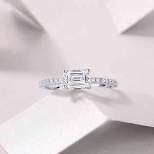 Elegant moissanite ring with emerald-cut center stone and pavé band in sterling silver.