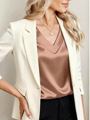 Lustrous satin V-neck blouse in champagne, worn with a cream blazer.