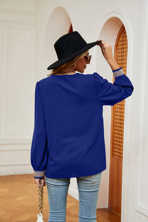 Royal blue blouson top with embroidered trim on cuffs and V-neck.