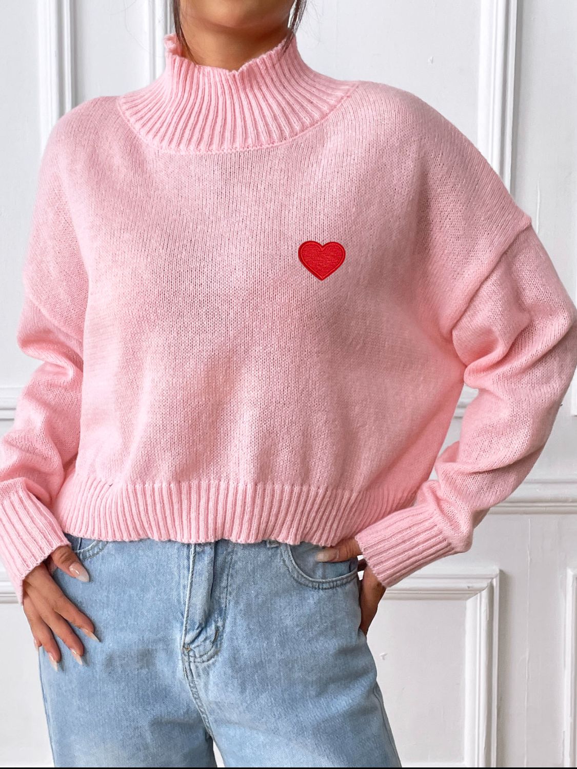 Blush pink cropped turtleneck knit sweater with embroidered red heart detail.
