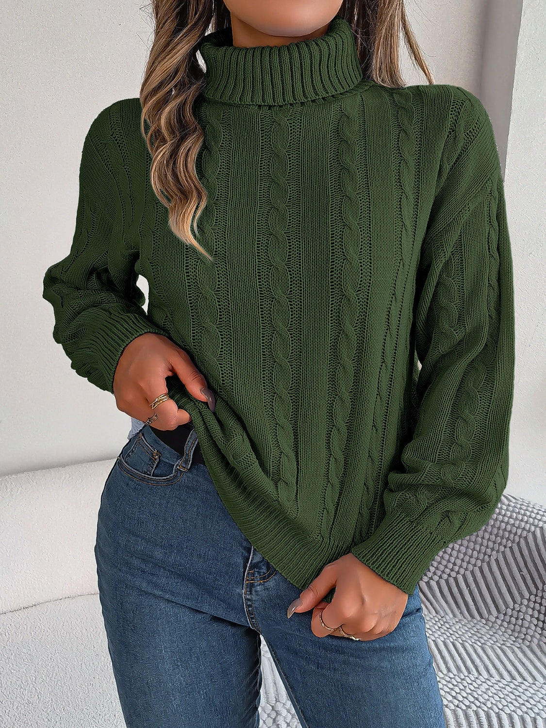 Dark green cable knit turtleneck sweater with voluminous sleeves and ribbed cuffs.