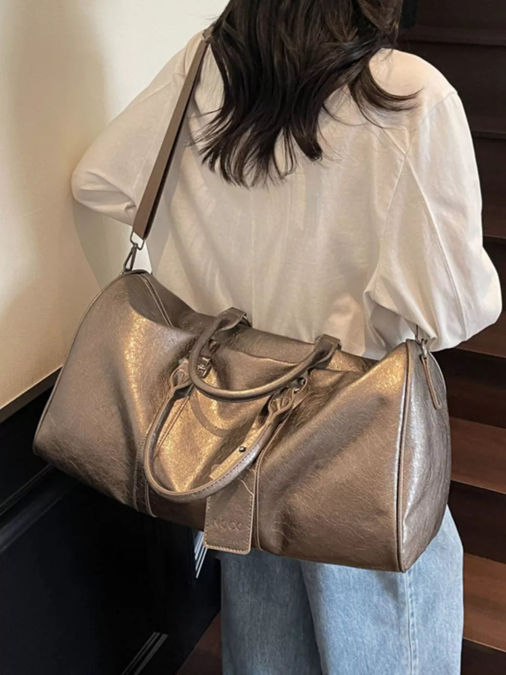 Textured metallic duffle bag in champagne color with top handles and detachable strap.