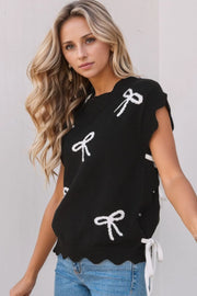 Black knit vest with white bow print, scalloped hem, and tie details.