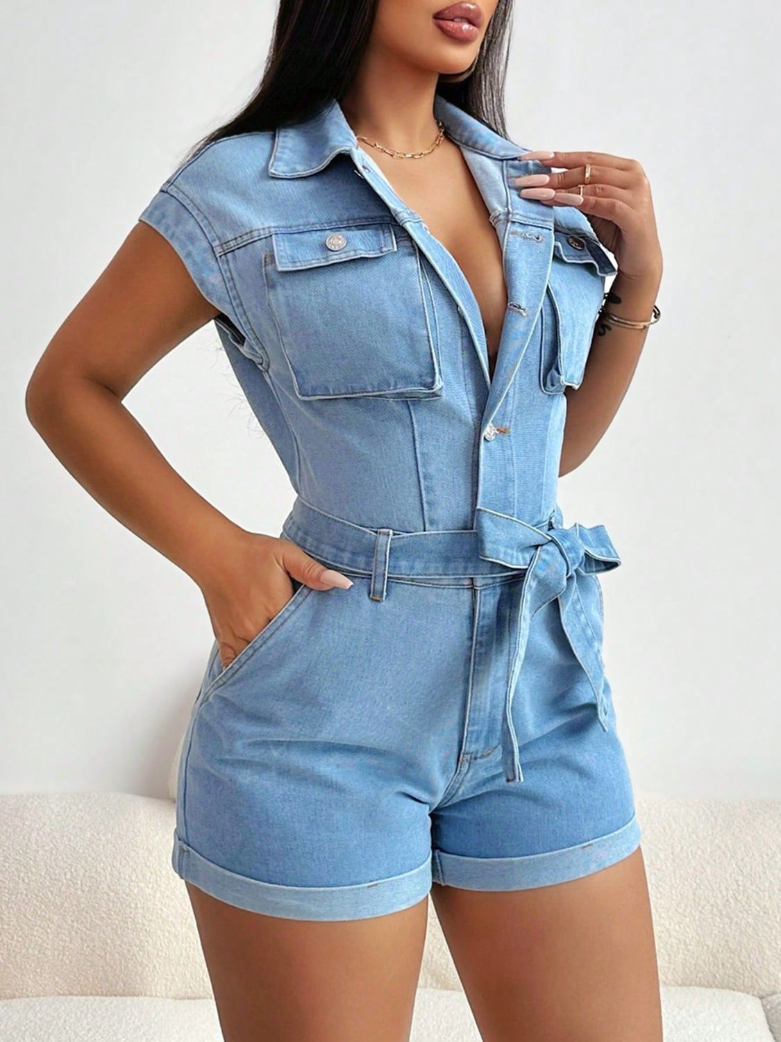 Light denim romper with short sleeves, chest pockets, and a tie waist.