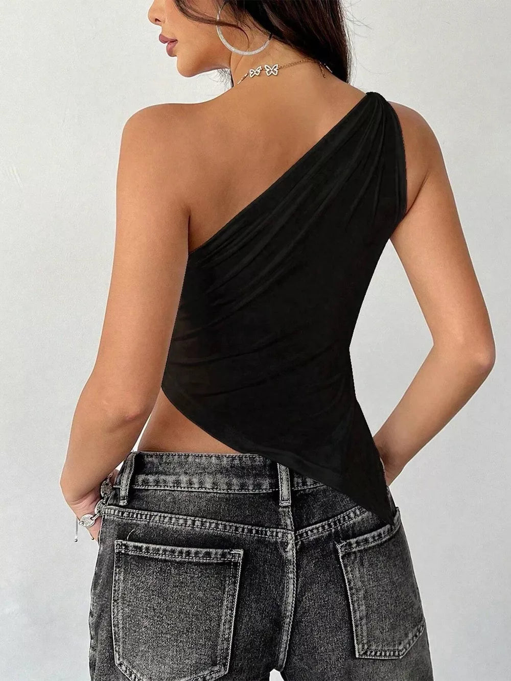 Black asymmetrical one-shoulder slim cami with draped detail, styled with jeans.