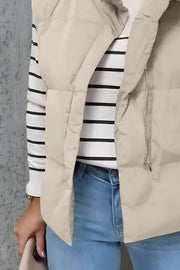 Padded beige stand collar vest with zipper detail over a striped long-sleeve shirt and jeans.