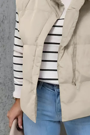 Padded beige stand collar vest with zipper detail over a striped long-sleeve shirt and jeans.