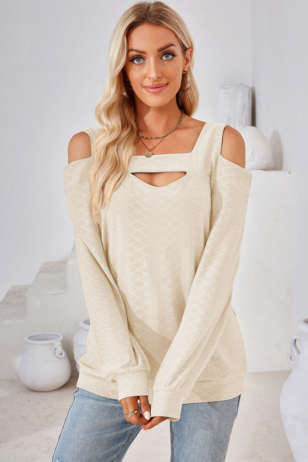 Cream geometric cutout shoulder top with square neckline and long sleeves.