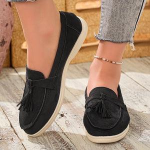 Black faux-suede slip-on loafers with decorative tassels and a comfortable sole.