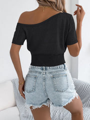 Black open-knit crop top with asymmetric neckline and short sleeves, styled with denim shorts.