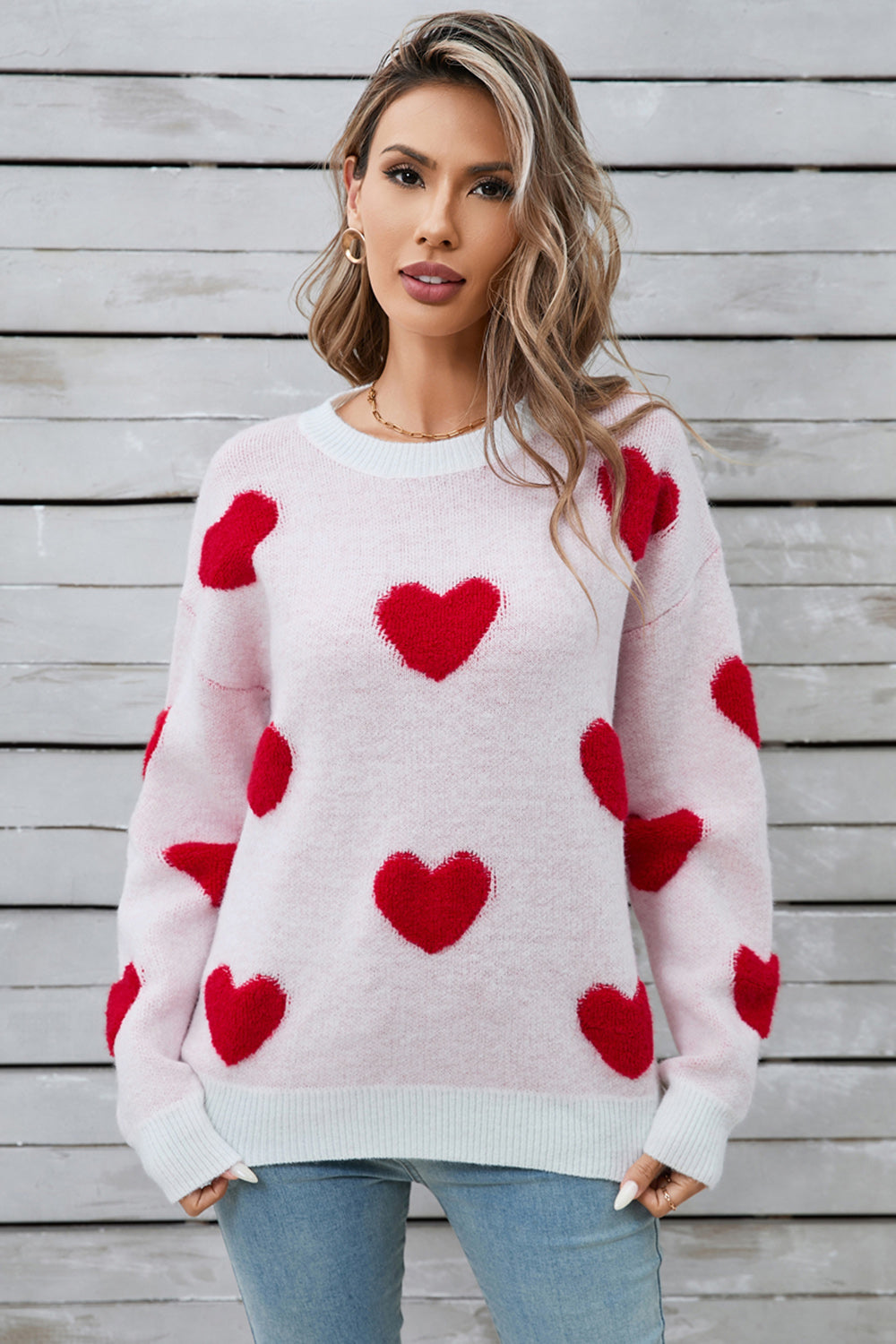 Light pink crewneck sweater with allover red heart appliqué, long sleeves, and ribbed cuffs and hem.