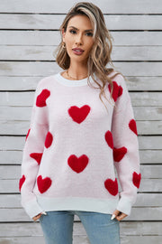 Light pink crewneck sweater with allover red heart appliqué, long sleeves, and ribbed cuffs and hem.