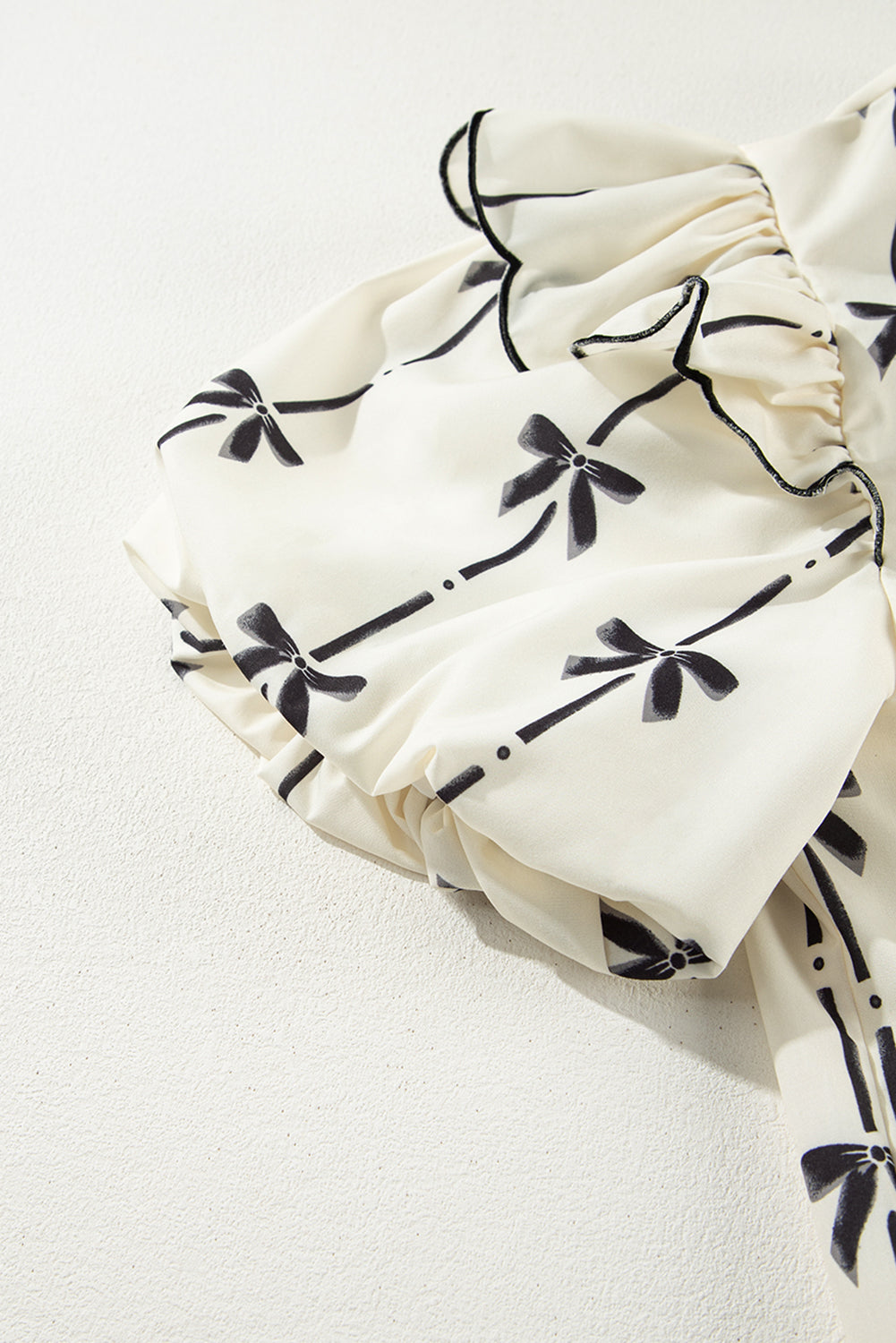 Ivory blouse with black bow print and ruffled sleeves.