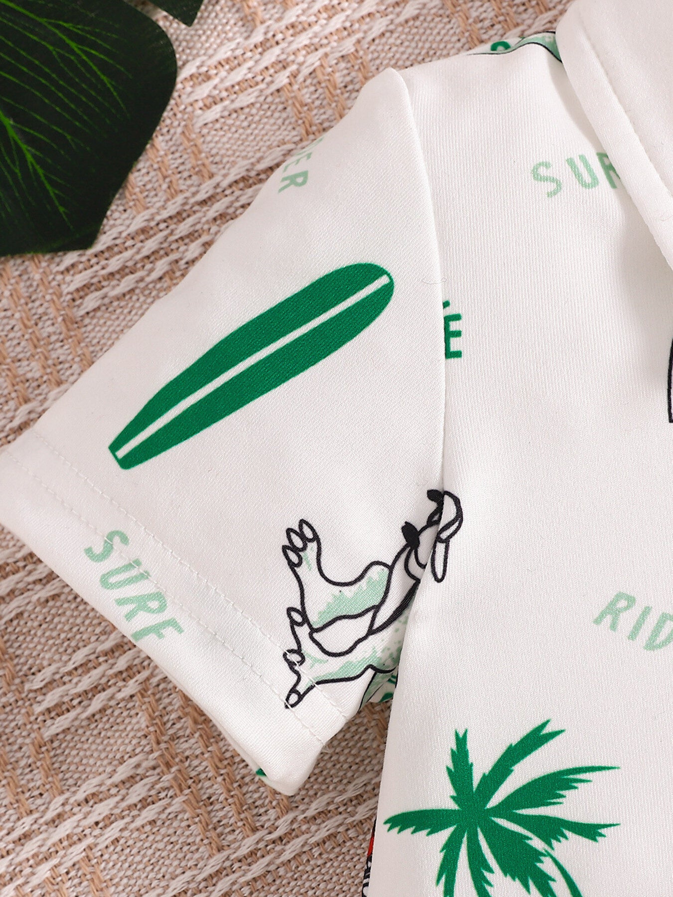 Baby polo shirt with white fabric, green dinosaur, surfboard, and palm tree print.
