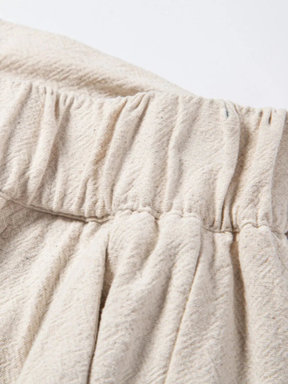 Beige linen drawstring trousers with elastic waistband and subtle herringbone texture.