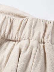 Beige linen drawstring trousers with elastic waistband and subtle herringbone texture.