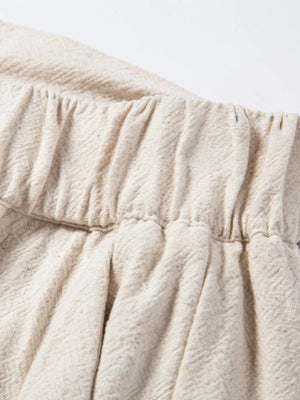 Beige linen drawstring trousers with elastic waistband and subtle herringbone texture.