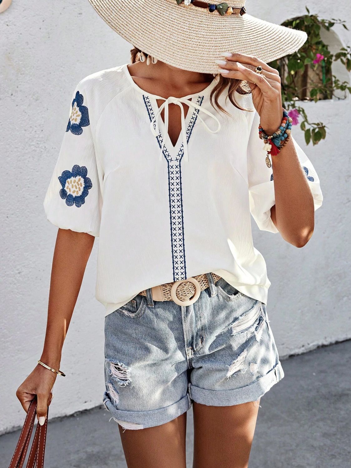 White embroidered yoke sleeve blouse with tie neck and blue floral details.