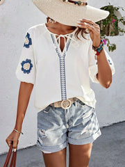 White embroidered yoke sleeve blouse with tie neck and blue floral details.