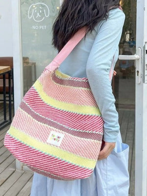 Vibrant striped woven shoulder bag in pink, yellow, and red with a pink strap.