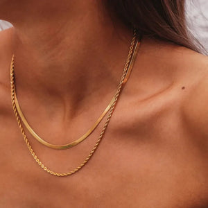Gold serpentine and rope chain necklace duo layered on a woman's décolletage.