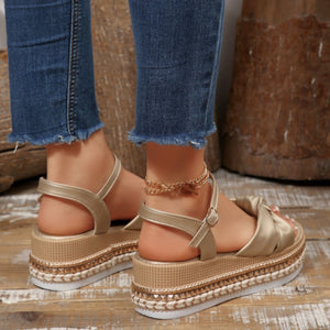 Gold bow knot wedge sandals with ankle buckle and braided trim, styled with frayed jeans.