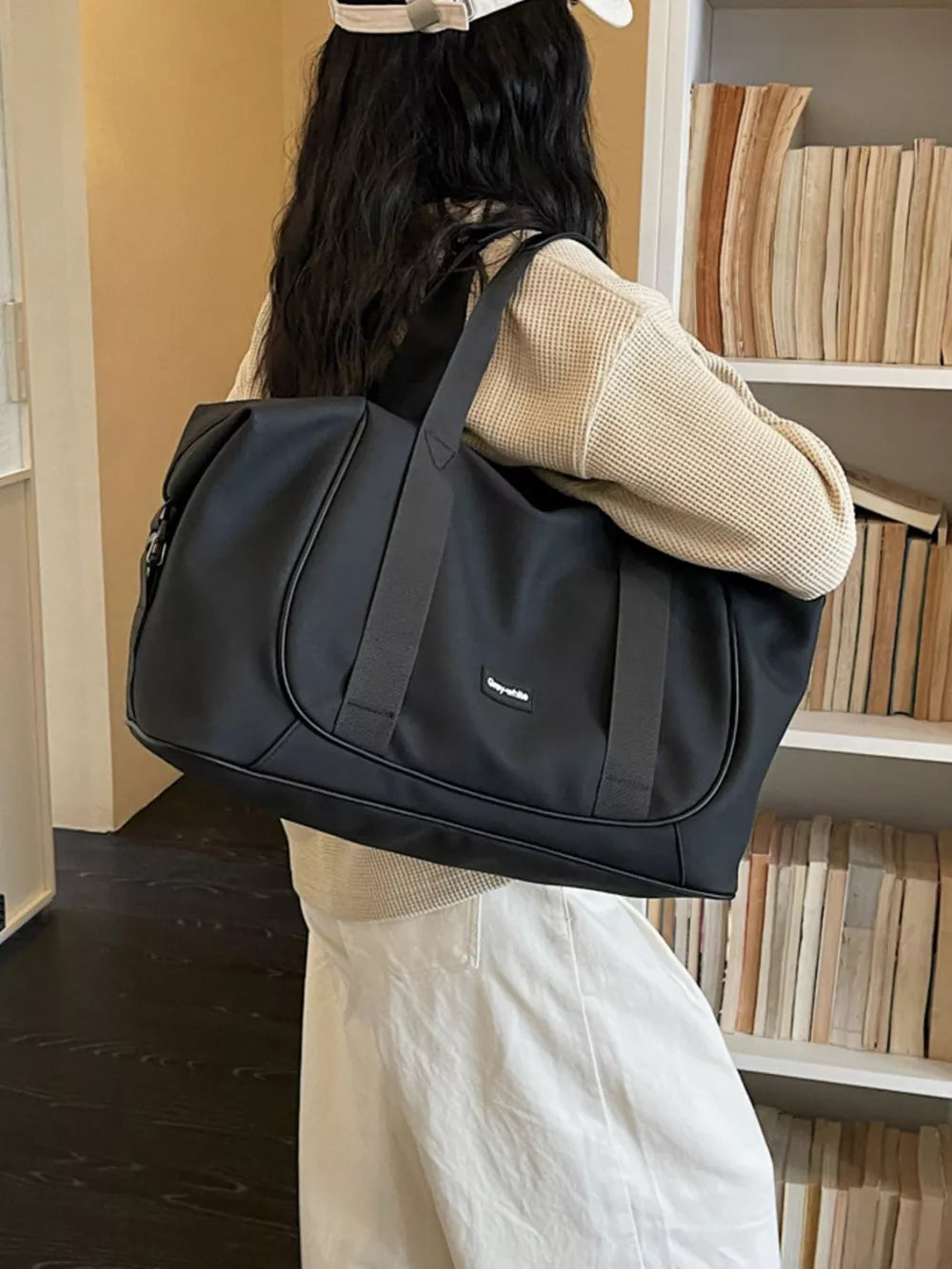 Black medium nylon travel duffle bag with adjustable strap and curved stitching detail.