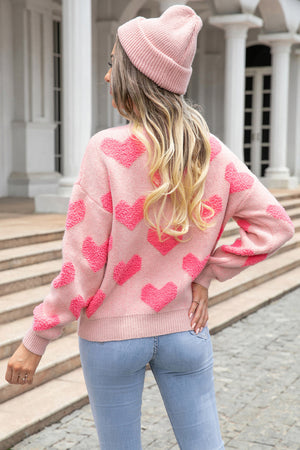 Blush pink knit pullover sweater with textured heart motif and ribbed cuffs.