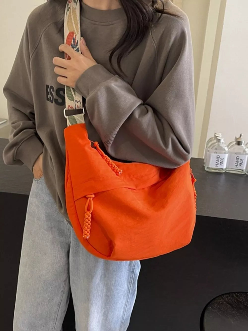 Orange woven strap small crossbody bag with braided zipper pulls.