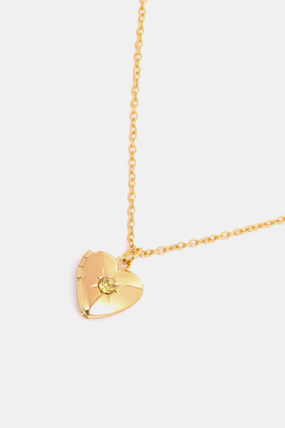 Gold heart locket necklace with a yellow gemstone and starburst detail on a delicate chain.