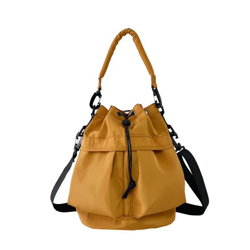 Mustard nylon drawstring bucket bag with top handle and crossbody strap.