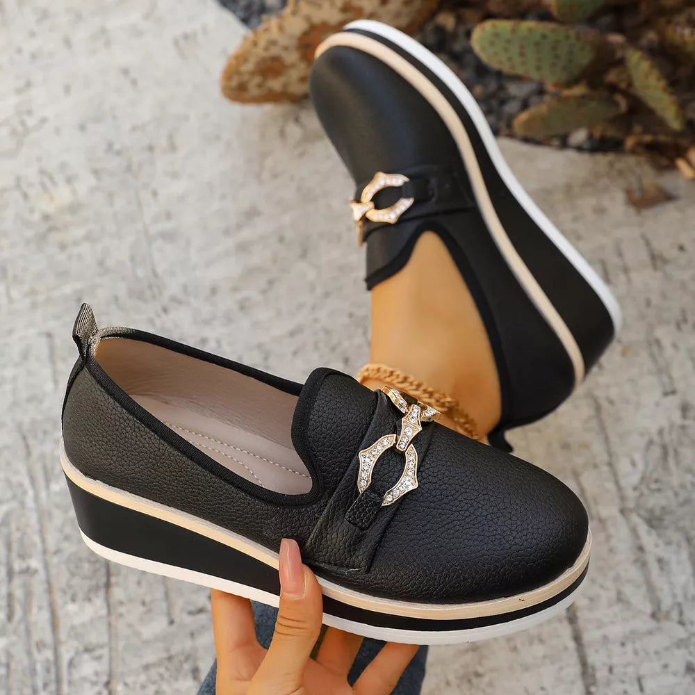Black wedge loafers with gold buckle detail and striped platform sole.