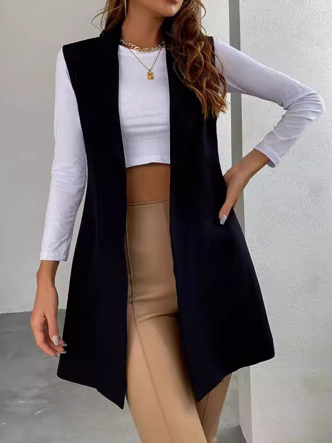 Black draped lapel vest with asymmetric hemline, styled open over a white top and tan pants.