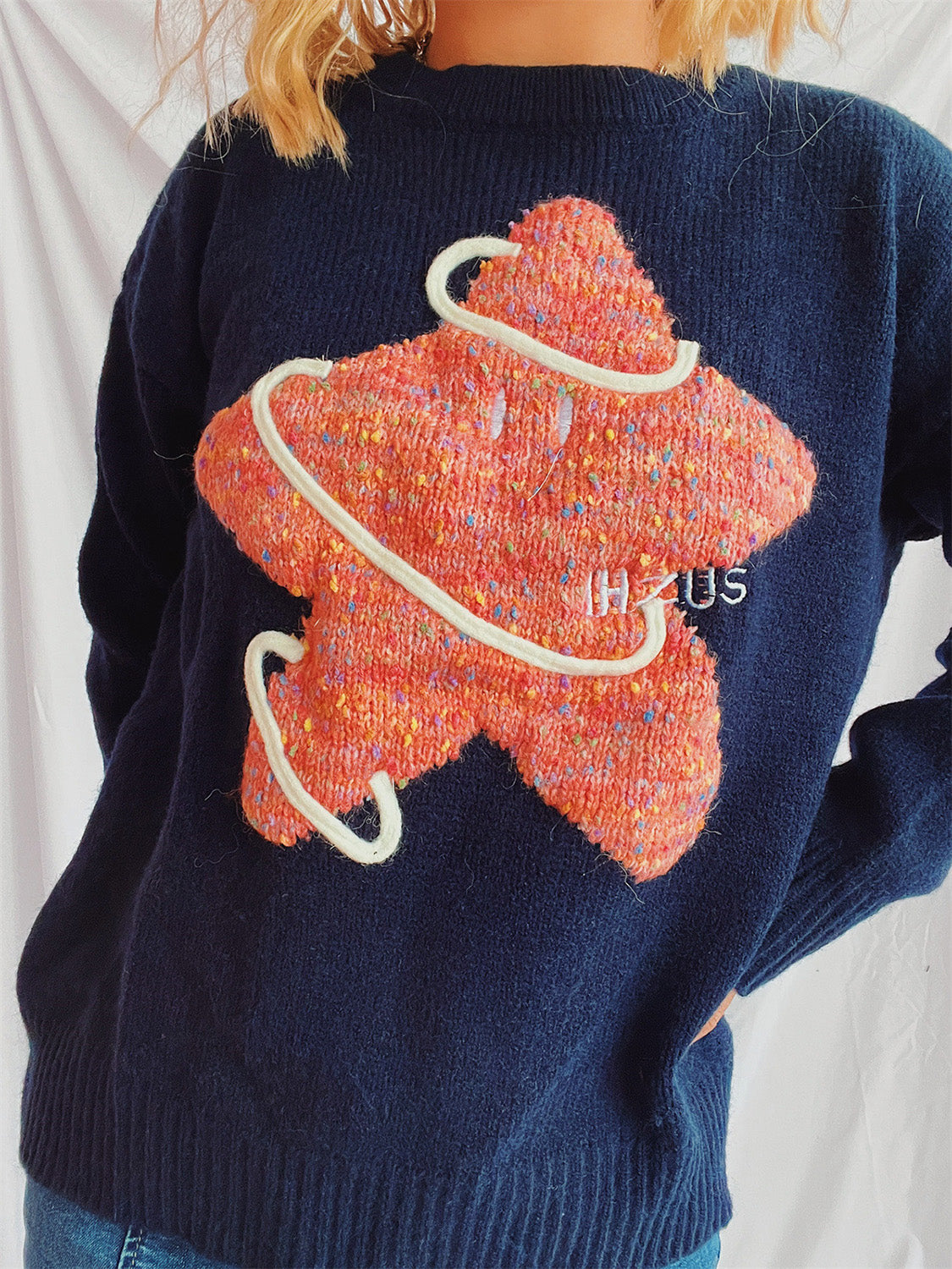 Navy knit jumper with textured orange starburst embroidery and white rope detail.