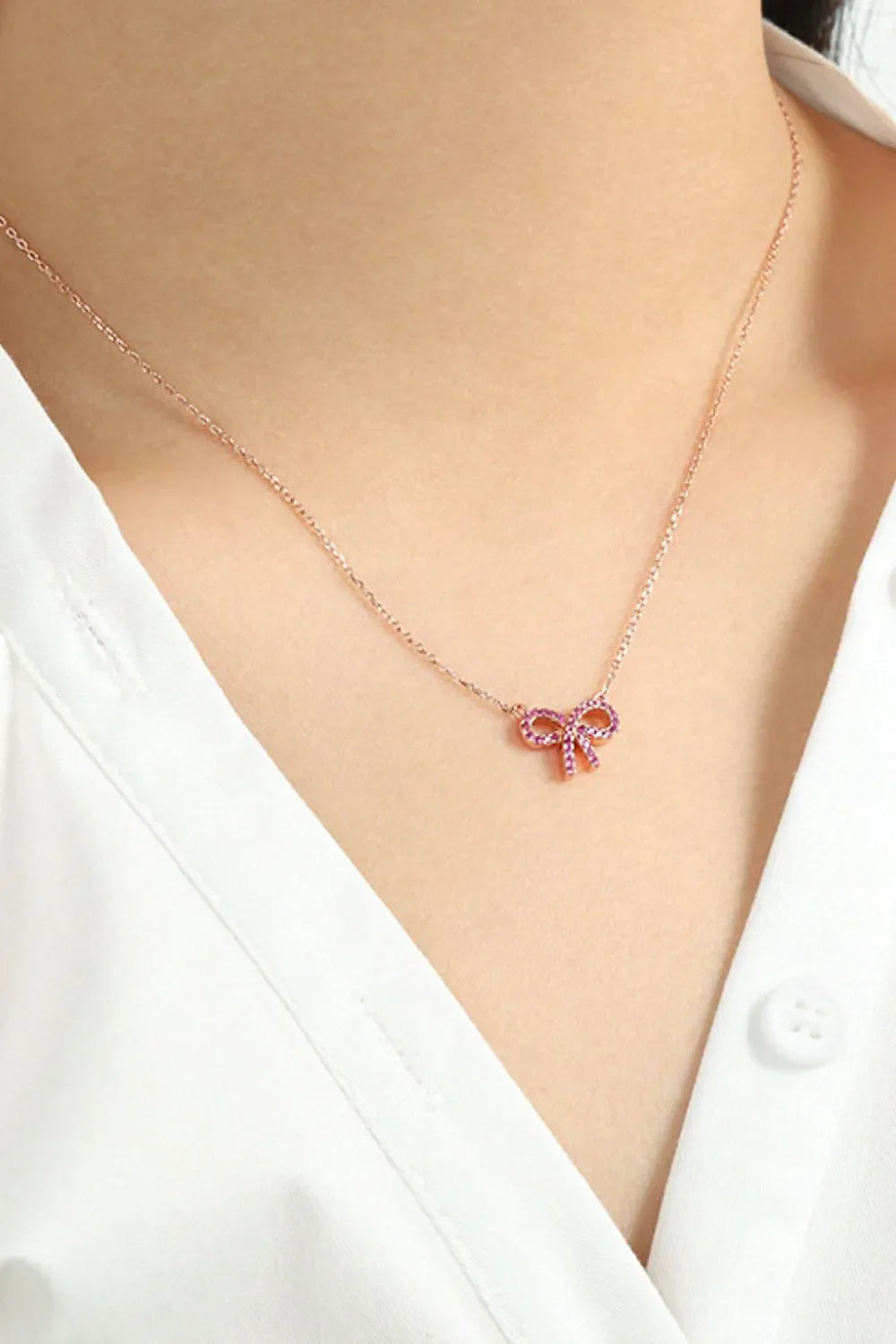 Rose gold bow pendant necklace with ruby-like embellishments on a delicate chain.