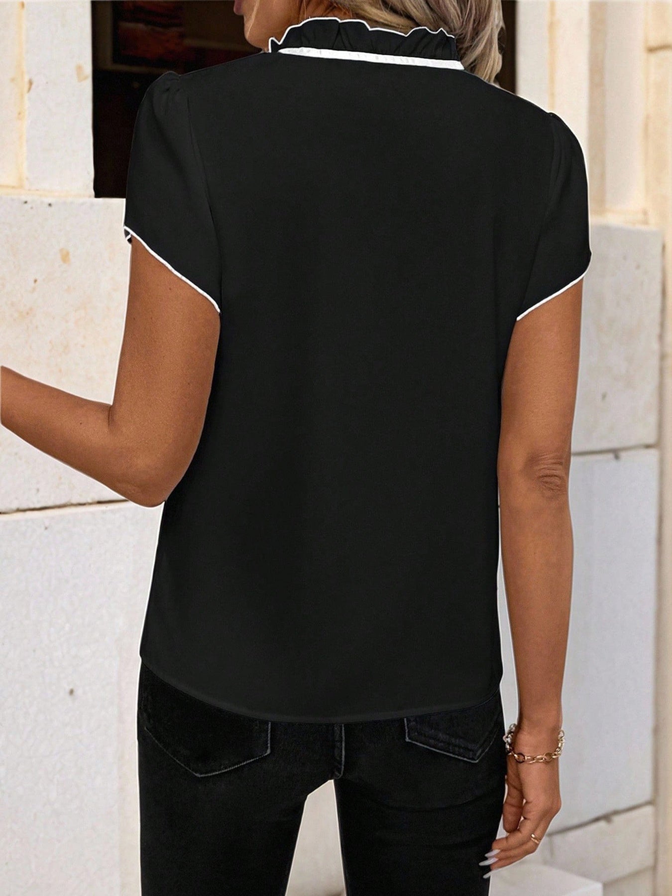 Black maternity blouse with white trim on ruffled tie-neck and short sleeves.
