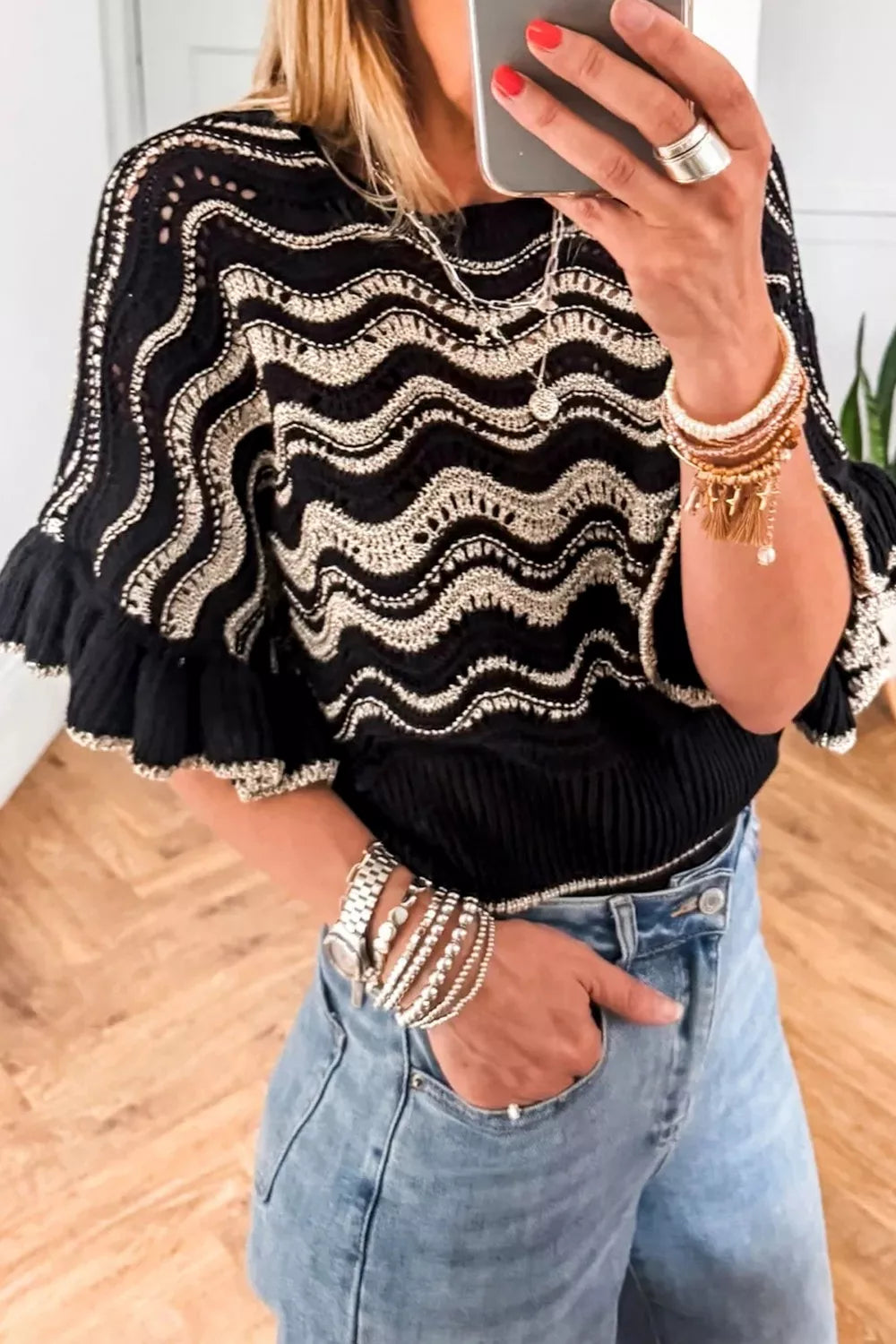 Black openwork knit sweater with metallic wave pattern and ruffled sleeves.